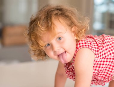 Dilini çıkarmış evde gülümseyen mavi gözlü güzel sarışın çocuğun.