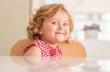 Oturan ve evde gülümseyen mavi gözlü güzel sarışın çocuğun.