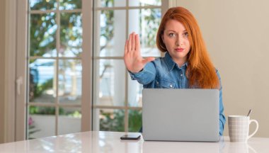 Kızıl saçlı kadın açık eliyle dur işareti ile ciddi ve kendine güvenen ifade, savunma hareketi yaparken bilgisayar dizüstü evde kullanma