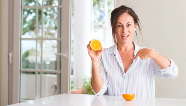 Middle Aged Woman Holding Orange Fruit Surprise Face Pointing Finger — Stock Photo, Image