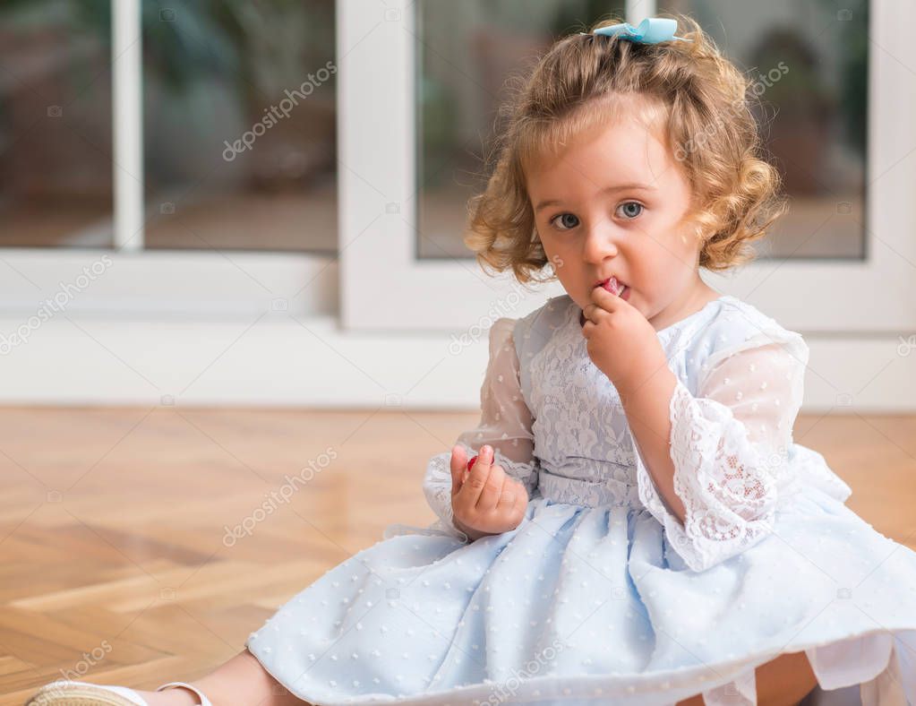 Beautiful blond child in a dress eating candy sitting on the floor at home