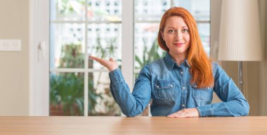 Gülümseyen Kızıl saçlı kadın evde neşeli sunulması ve kameraya bakarak avucunun ile işaret.