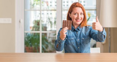 Çikolata bar evde ok işareti, başparmak ile parmak, mükemmel işareti yapıyor kocaman bir gülümseme ile mutlu tutan Kızıl saçlı kadın