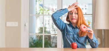 Kızıl saçlı kadın seçer apple ve kafasına, utanç ve sürpriz yüz ile şok el ile vurguladı çörek arasında öfkeli ve sinirli. Korku ve hata için üzgün.