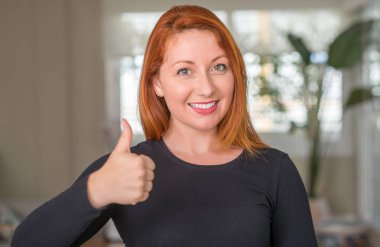 Kızıl saçlı kadın, kocaman bir gülümseme ile ok işareti yapıyor mutlu ev, parmaklarıyla, mükemmel işaret parmak