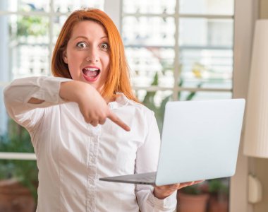 Ev çok mutlu el ve parmak ile işaret bilgisayar dizüstü kullanan Kızıl saçlı kadın