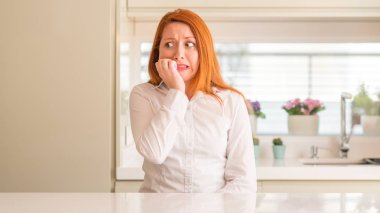 Kızıl saçlı kadın stresli ve gergin ile mutfak at tırnak ısırma dudaklarından eller. Anksiyete sorunu.
