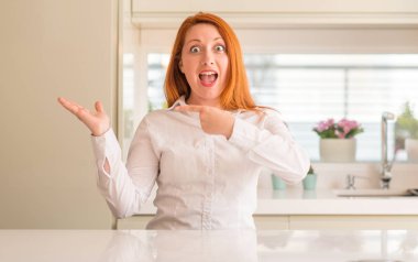 Kızıl saçlı kadın hayrete ve el ile sunulması ve parmak ile işaret ederken kameraya gülümseyen mutfak at.