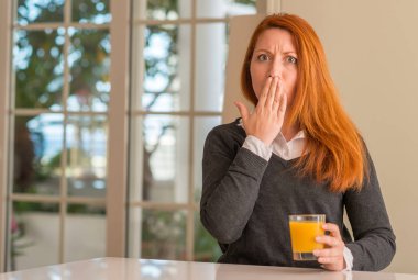 Kızıl saçlı kadın holding portakal suyu cam evde, hata, korku, sessizlik içinde gizli kavramı korkmuş ifade için utanç ile kapak ağız el ile şok