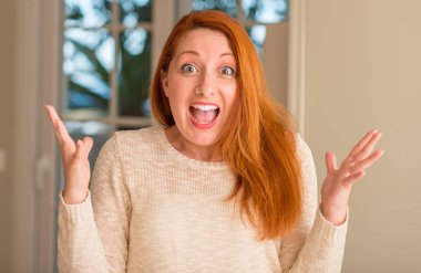 Kızıl saçlı kadın evde çok mutlu ve heyecanlı, kocaman bir gülümseme ile çığlık ve ellerini kaldırdı zaferini kutluyor kazanan ifade