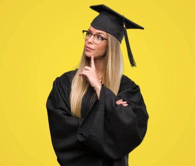 Gözlük ve Mezuniyet cübbesi ciddi bir yüz düşünme hakkında soru, çok karışık bir fikir giyen güzel genç kadın