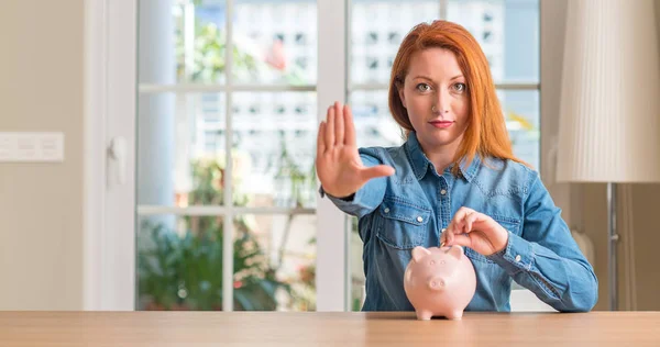 Rödhårig Kvinna Sparar Pengar Spargrisen Hemma Med Öppen Hand Gör — Stockfoto