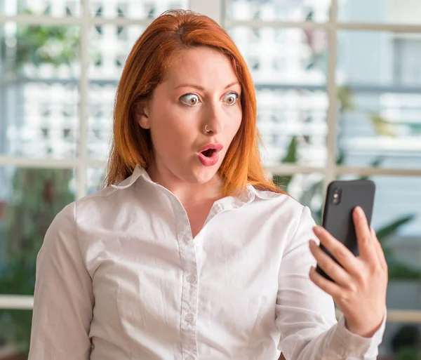Κοκκινομάλλης Γυναίκα Χρησιμοποιώντας Smartphone Στο Σπίτι Φοβισμένος Κατάσταση Σοκ Πρόσωπο — Φωτογραφία Αρχείου