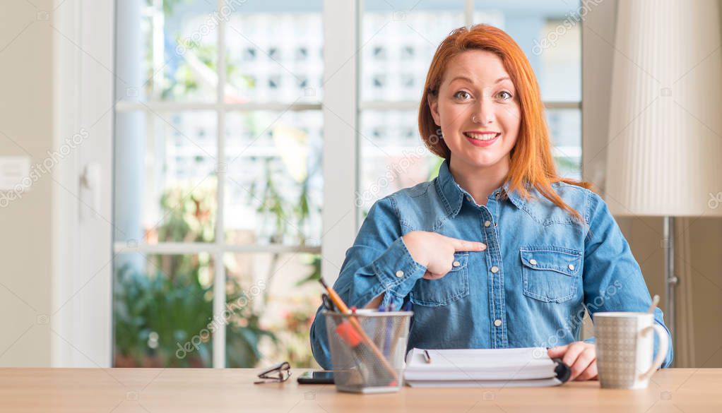 Redhead woman studying at home with surprise face pointing finger to himself