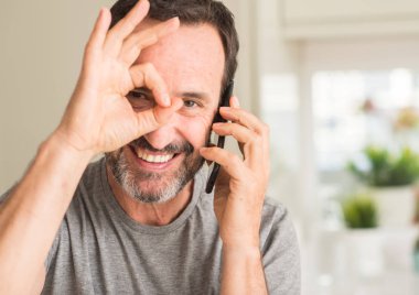 Mutlu yüz el parmaklarının arasından seyir göz üzerinde ok işaretiyle yapıyor gülümseyen ile akıllı telefon kullanan orta yaş adam