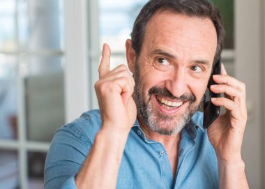 Smartphone sürpriz bir fikirle kullanan yaş adam orta veya gülen yüz, bir numara ile işaret parmağı soru