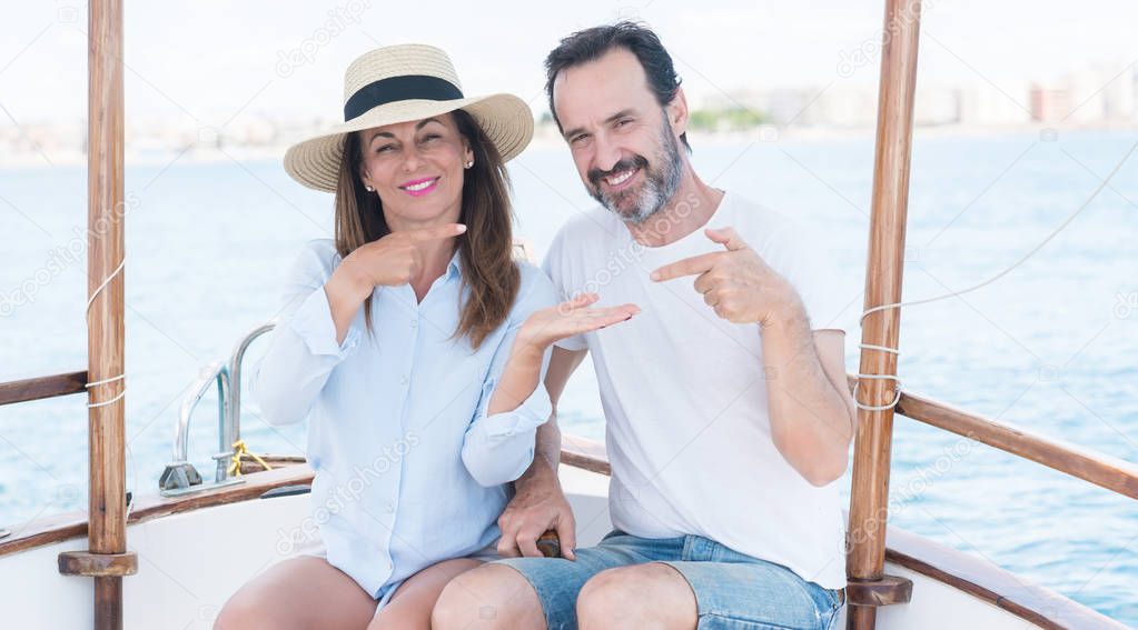 Middle age couple traveling on sailboat very happy pointing with hand and finger