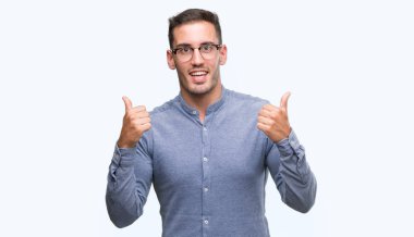 El ile pozitif jest yapıyor gözlük başarı işareti giyiyor zarif yakışıklı genç gülümseyen ve mutlu yaşasın. Neşeli bir ifadeyle, kazanan jest kameraya bakıyor.