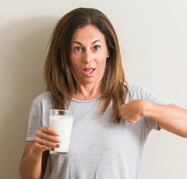 中年妇女喝一杯新鲜的牛奶与惊讶的脸指向自己的手指 — 图库照片