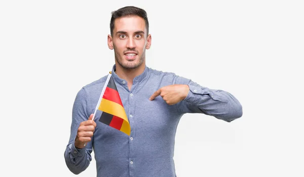 自分自身に驚き顔人差し指とドイツの国旗を保持しているハンサムな若い男 — ストック写真