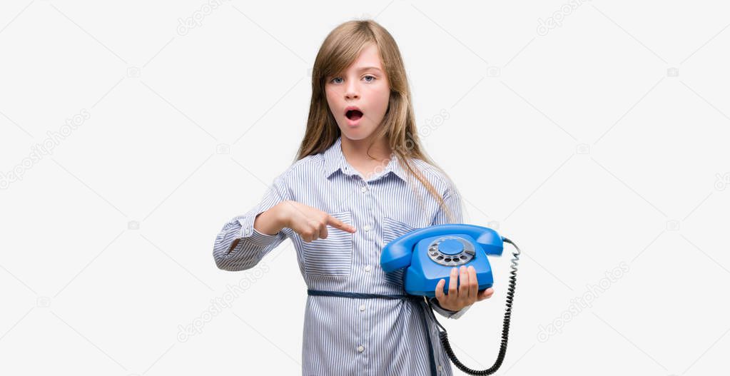 Young blonde toddler holding vintage telephone very happy pointing with hand and finger