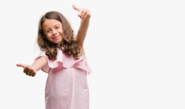 Onaylama pembe elbise giymiş esmer Latin kız el ile pozitif jest yapıyor gülümseyen ve başarı için mutlu yaşasın. Kamera, kazanan jest arıyorsunuz.