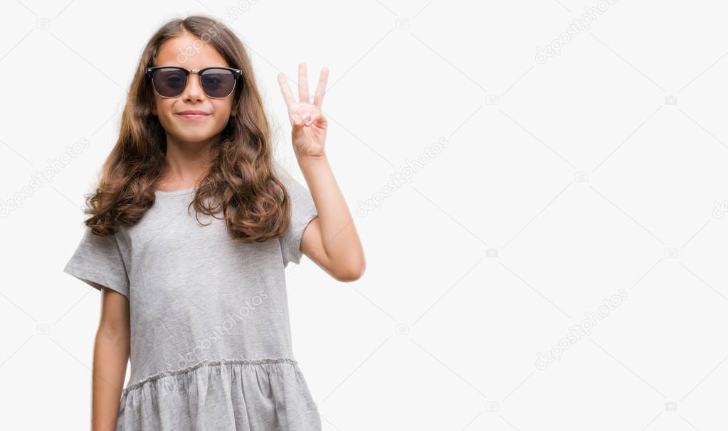 Brunette hispanic girl wearing sunglasses showing and pointing up with fingers number three while smiling confident and happy.