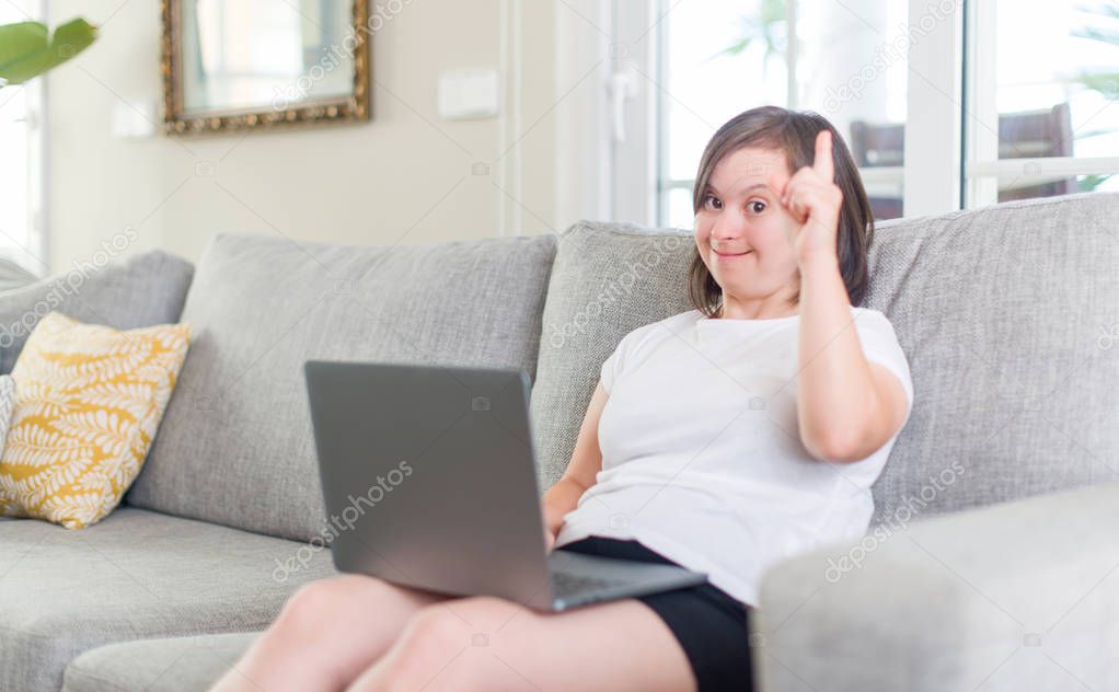 Down syndrome woman at home using computer laptop surprised with an idea or question pointing finger with happy face, number one