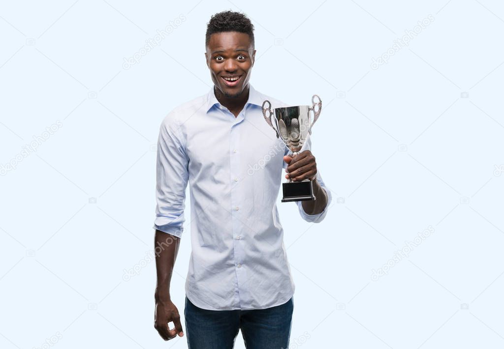 Young african american man holding trophy with a happy face standing and smiling with a confident smile showing teeth