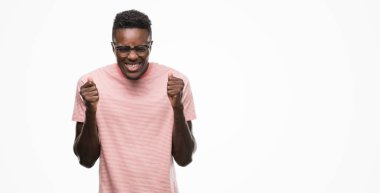 Silah ile başarı için t-shirt heyecanlı pembe giyen genç Afro-Amerikan adam zafer kutluyor gülümseyen kaldırdı. Kazanan kavramı.