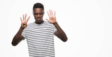 Gözlük ve gösterilen ve parmakları ile işaret lacivert t-shirt giyen genç Afro-Amerikan adam numara 9 kendinden emin ve mutlu gülümseyerek süre.