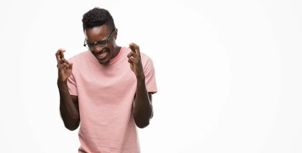 年轻的非洲裔美国人穿着粉红色 T恤微笑着交叉手指 希望和眼睛闭上 运气和迷信概念 — 图库照片