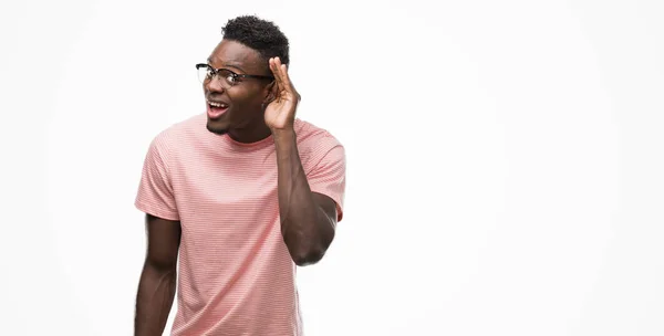 年轻的非洲裔美国人穿着粉红色 T恤微笑着用手在耳边听着谣言或流言蜚语 耳聋概念 — 图库照片