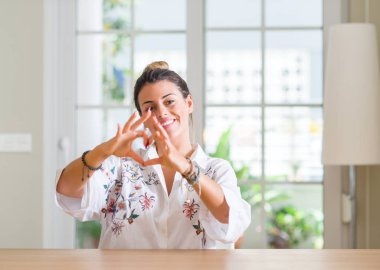 Gülümseyen genç kadın evde kalp simgesi ve elleriyle şekil gösterilen aşık. Romantik kavramı.