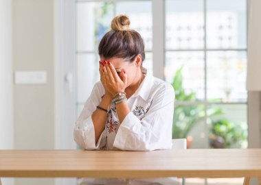 Genç kadın evde yüz eller ile ağlayarak süre kapsayan üzgün ifade ile. Depresyon kavramı.