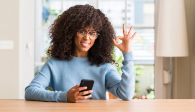 Parmak, mükemmel sembolü ile ok işareti yapıyor smartphone kullanarak güzel bir Afrikalı-Amerikalı kadın