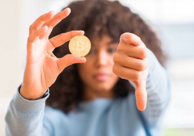 Afrikalı-Amerikalı kadın holding altın bitcoin cryptocurrency evde kızgın yüzü ile negatif antipati başparmak aşağı, ret kavramı ile gösterilen işareti