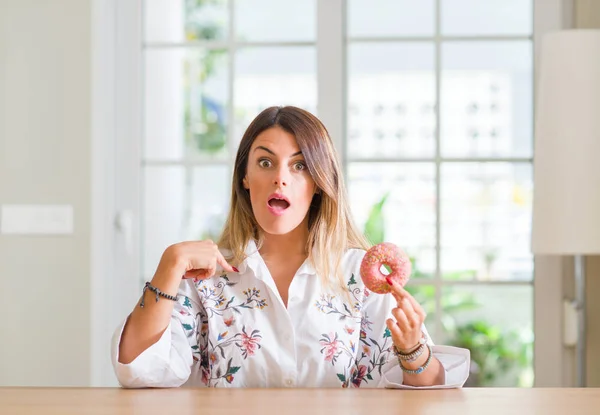 Mujer Joven Casa Comiendo Donut Con Cara Sorpresa Señalando Dedo — Foto de Stock