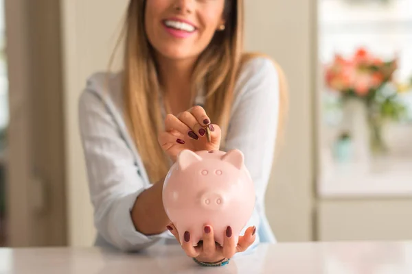 Hermosa Joven Sonriendo Sosteniendo Una Moneda Invirtiendo Una Alcancía Casa —  Fotos de Stock