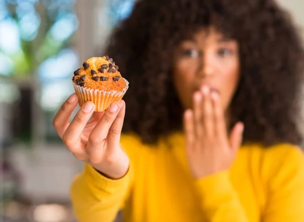 非洲裔美国妇女拿着巧克力松饼捂着嘴 手里拿着羞愧的错误 恐惧的表情 沉默中恐惧 秘密概念 — 图库照片