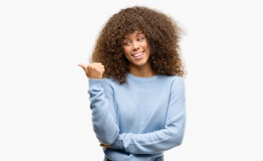 Seyir ve başparmak yanında yukarıyı mutlu yüz ile gülümseyen bir kazak giyen Afrikalı-Amerikalı kadın.