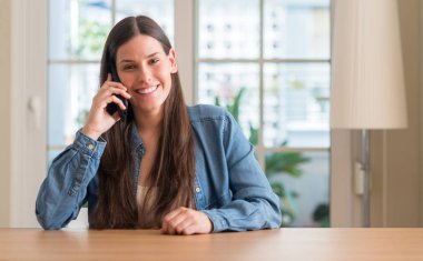 Ayakta ve diş gösterilen kendine güvenen bir gülümsemeyle gülümseyerek mutlu bir yüz ile akıllı telefon kullanan genç kadın