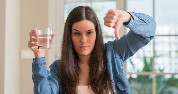 年轻女子喝杯水在家中与愤怒的脸 消极的迹象显示不喜欢拇指下来 拒绝概念 — 图库照片