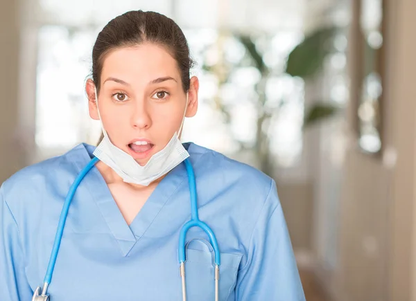 Young nurse woman wearing mask and stethoscope scared in shock with a surprise face, afraid and excited with fear expression