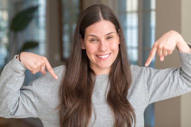 Genç güzel kadın evde kendini gururlu ve mutlu parmakları ile işaret emin yüz, gülümseme ile seyir.