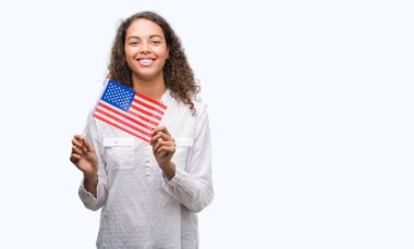 Estates Amerika bayrağı ile ayakta ve diş gösterilen kendine güvenen bir gülümsemeyle gülümseyerek mutlu bir yüz tutan genç İspanyol kadın