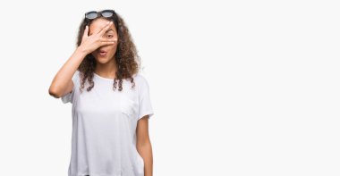 Mahcup ifadeyle parmaklarımın arasından yüz ve gözler el ile kapsayan şok bakmak güneş gözlüğü takmış genç İspanyol kadın arıyor.