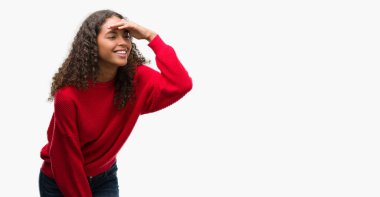 Kırmızı kazaklı çok mutlu ve gülümseyen uzakta el ile üzerine kafa seyir giyen genç İspanyol kadın. Arama kavramı.