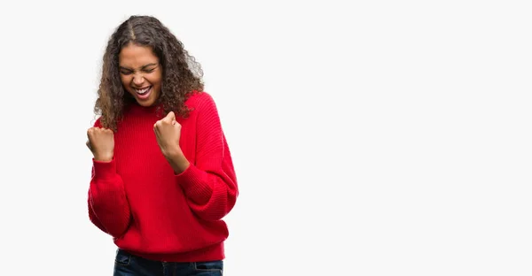 年轻的西班牙裔妇女穿着红色毛衣非常高兴和兴奋做赢家手势与手臂举起 微笑和尖叫的成功 庆祝概念 — 图库照片