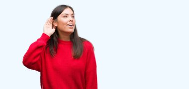 Genç güzel İspanyol bir işitme söylenti ya da dedikodu için dinleme kulak üzerinde el ile gülümseyen kırmızı kazak giyiyor. Sağırlık kavramı.